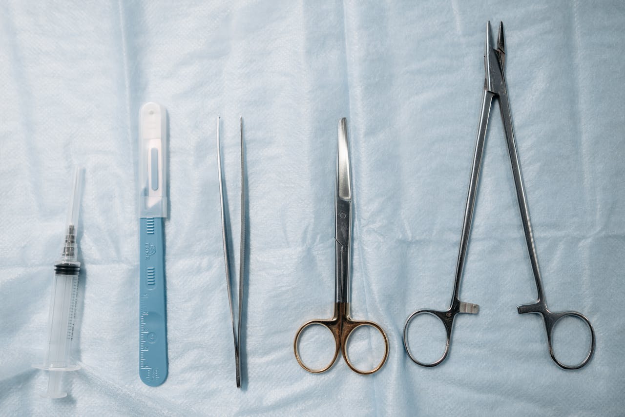 Flat lay of surgical tools including scissors, forceps, and syringe on a sterile blue cloth.